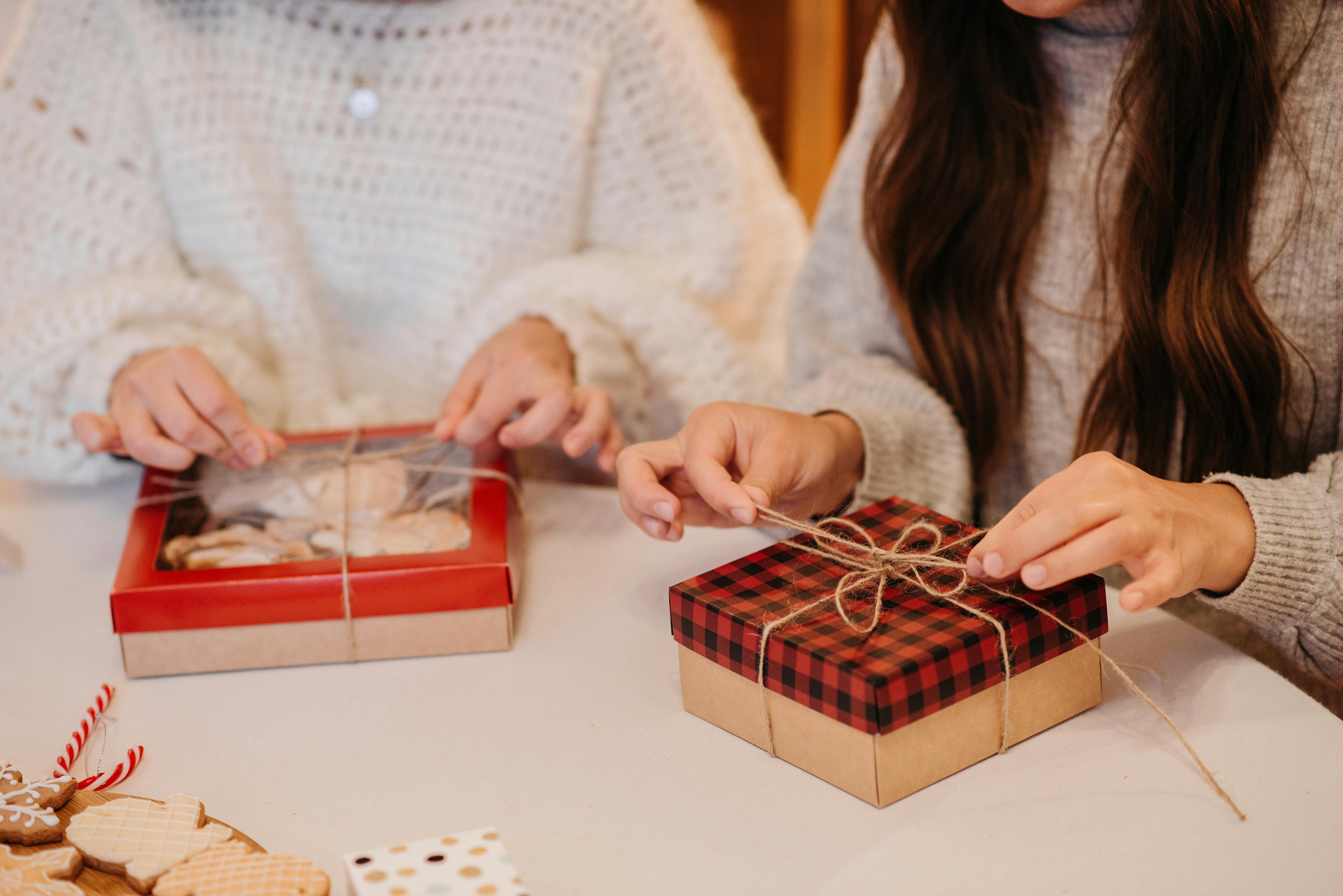 Two people wrapping Christmas cookies as holiday gifts in a cozy indoors setting.