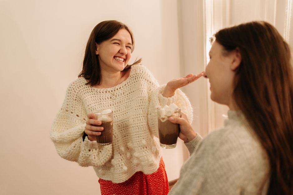 Two women enjoying chocolate drinks indoors, sharing smiles and laughter.