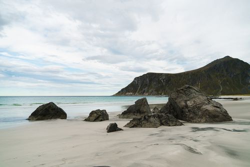 Free Remote empty coast with huge boulders and green mountain ridge on background in clouds Stock Photo