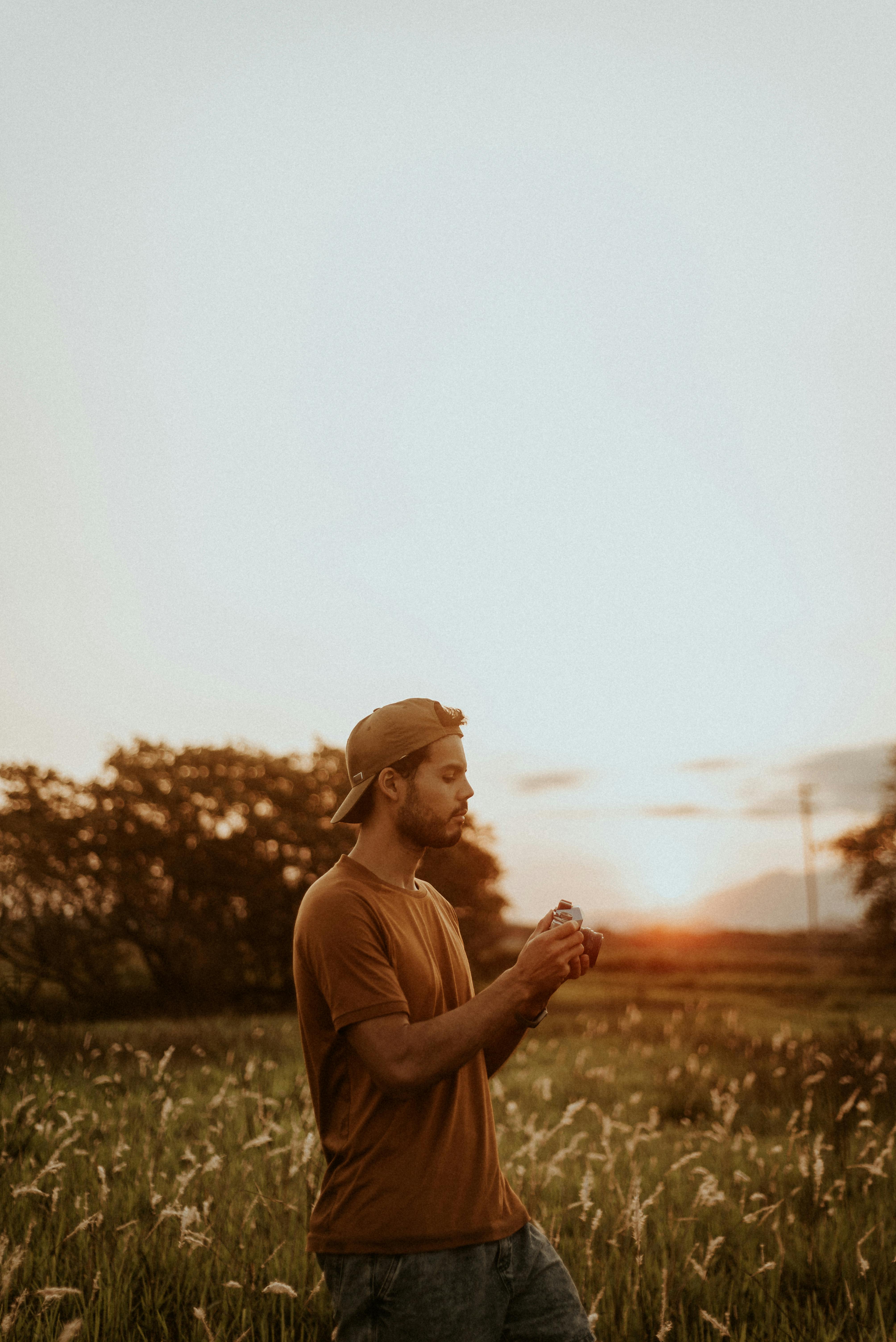 A young man stands in a field during sunset, embracing nature's tranquility.