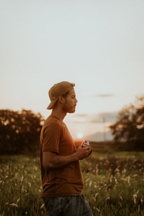 Free Man in Brown Crew Neck T-shirt and Brown Hat Standing on Green Grass Field  Stock Photo