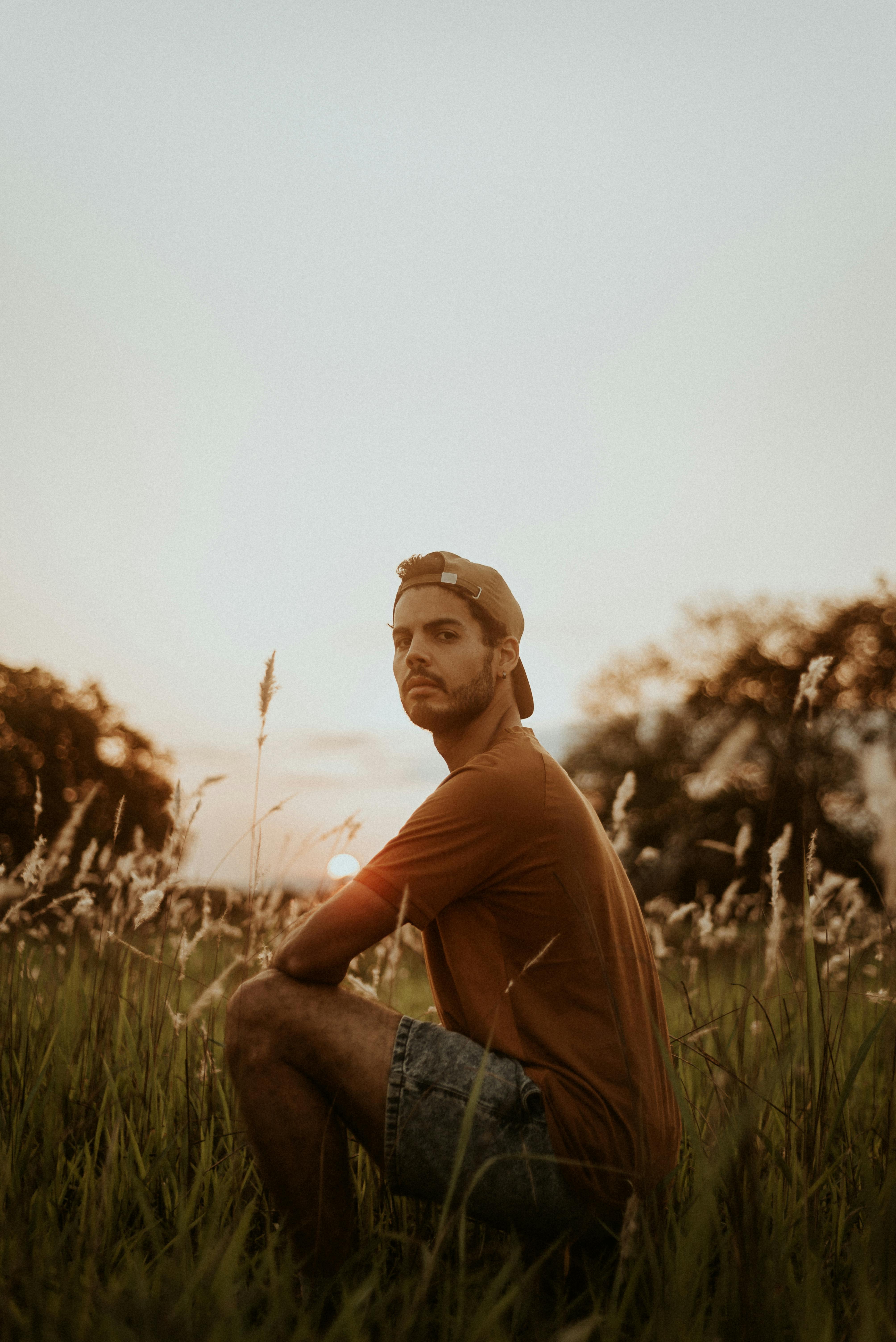 man in crew neck t shirt and denim shorts sitting on green grass field