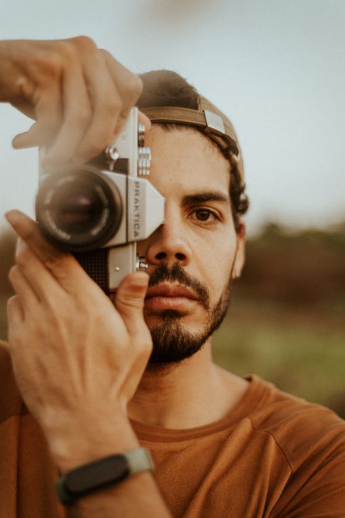Free Bearded man captures a moment with vintage camera in an outdoor setting. Stock Photo
