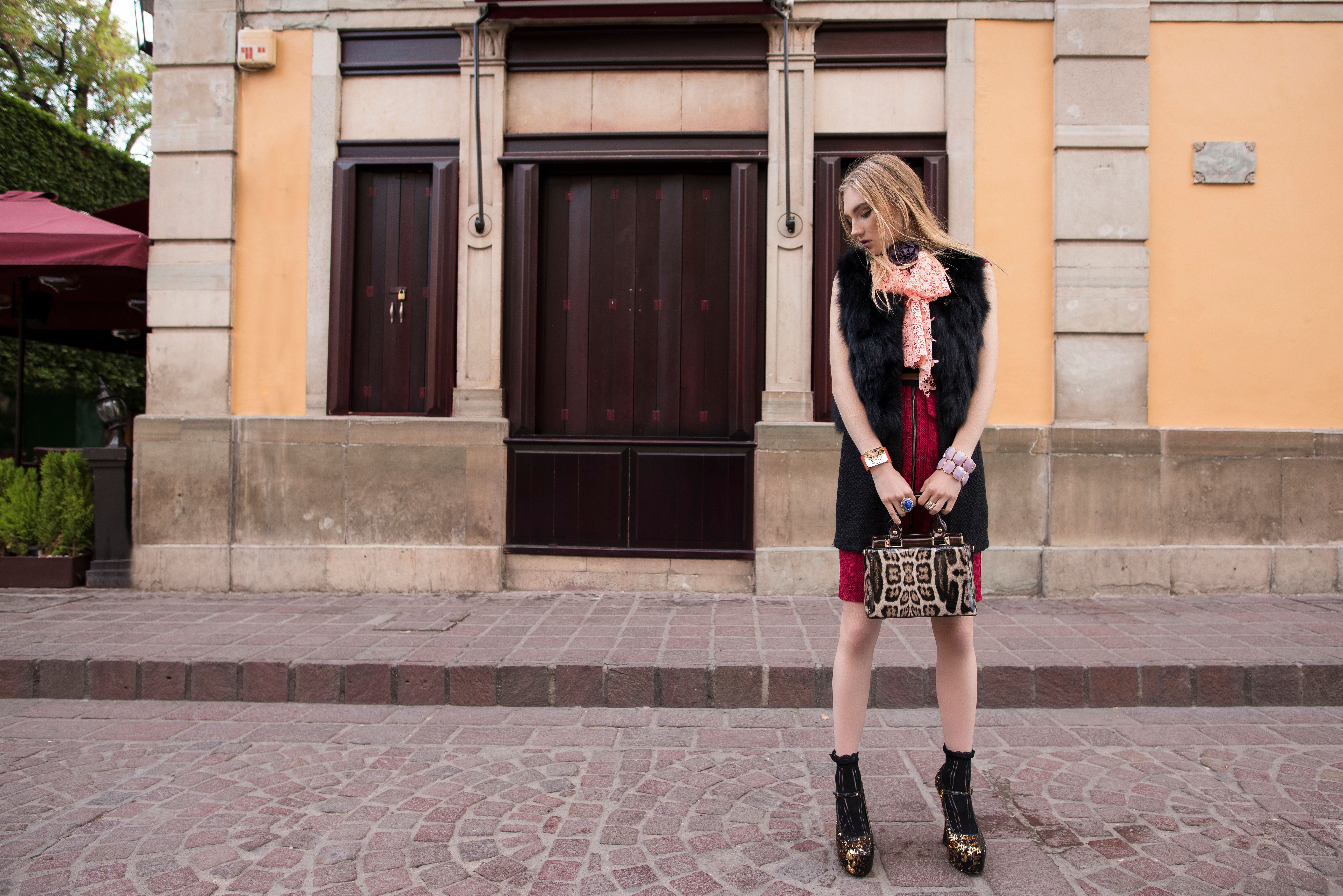 Stylish woman with leopard print bag poses in front of an old building.
