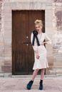 Photo of Woman in White Long Sleeve Dress Standing in Front of Brown Wooden Door
