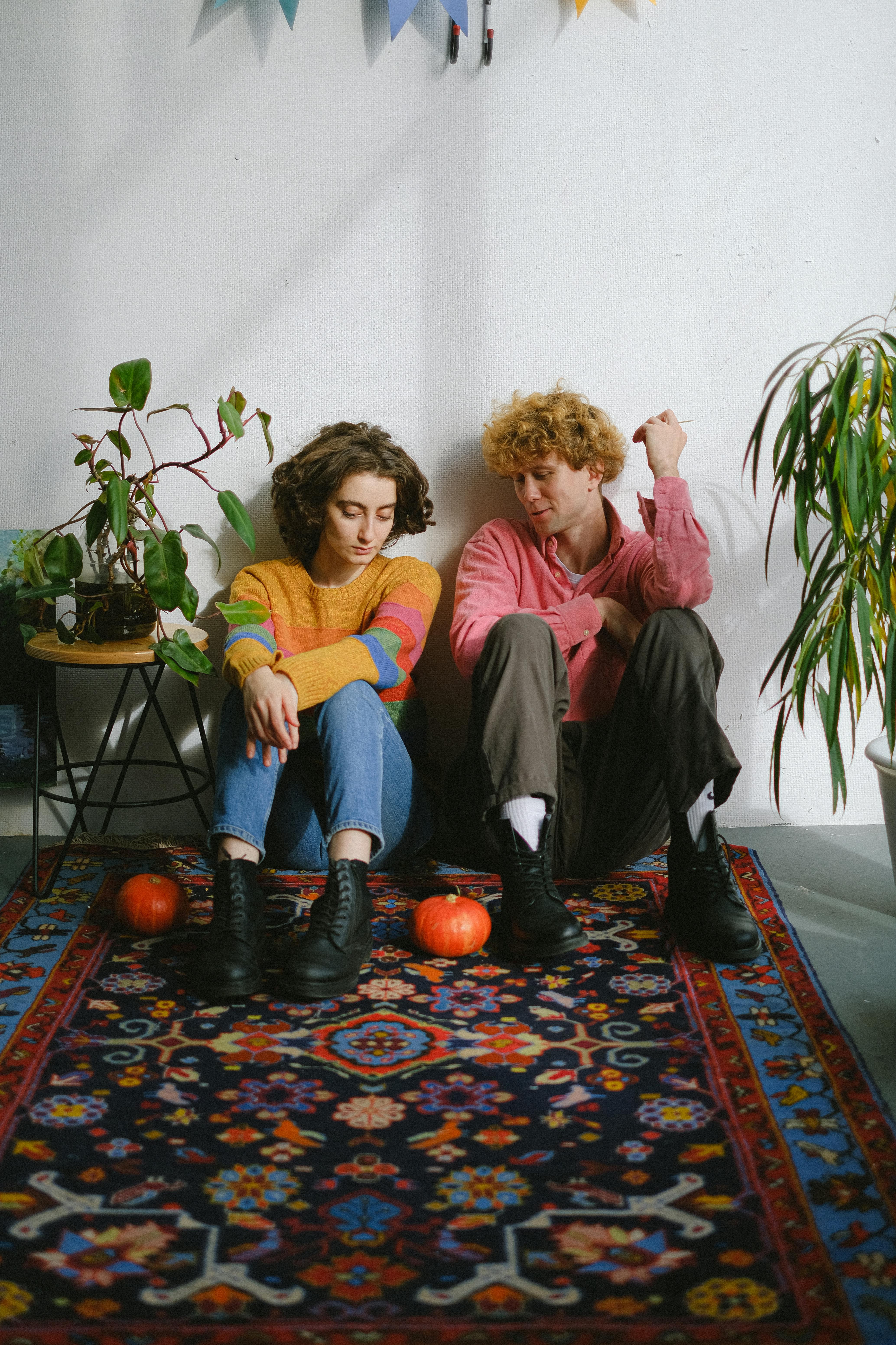 一对年轻夫妇坐在复古地毯上，地毯上铺着南瓜，营造出舒适的秋季氛围