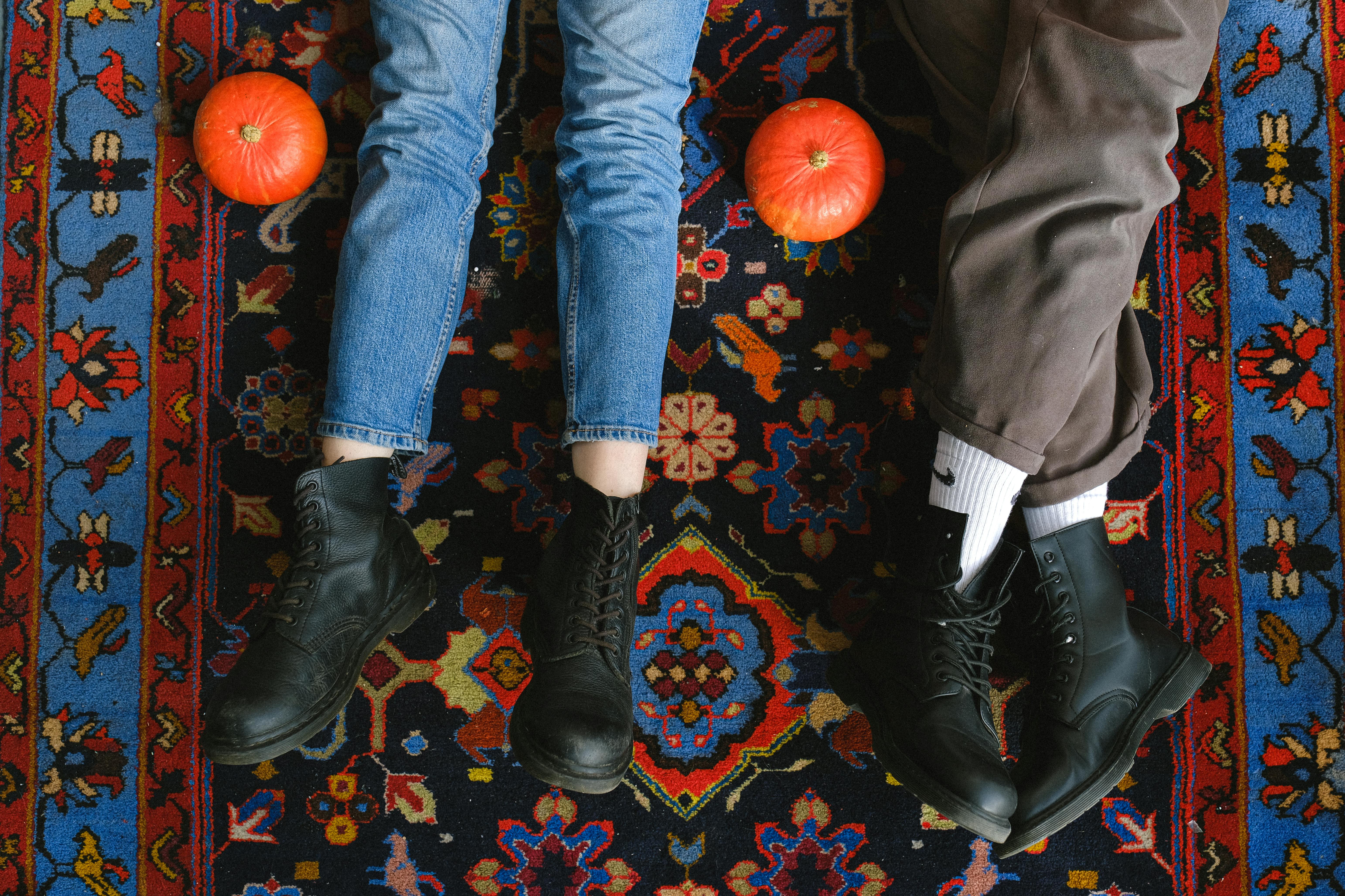 两双脚穿着皮靴，躺在两侧摆着南瓜的充满活力的地毯上