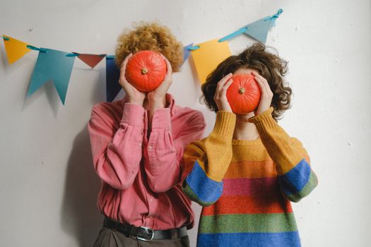 Two people holding pumpkins cover faces in a colorful and playful scene.