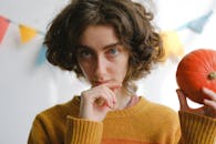 一幅以节日为背景的妇女肖像，她穿着毛衣，手拿南瓜