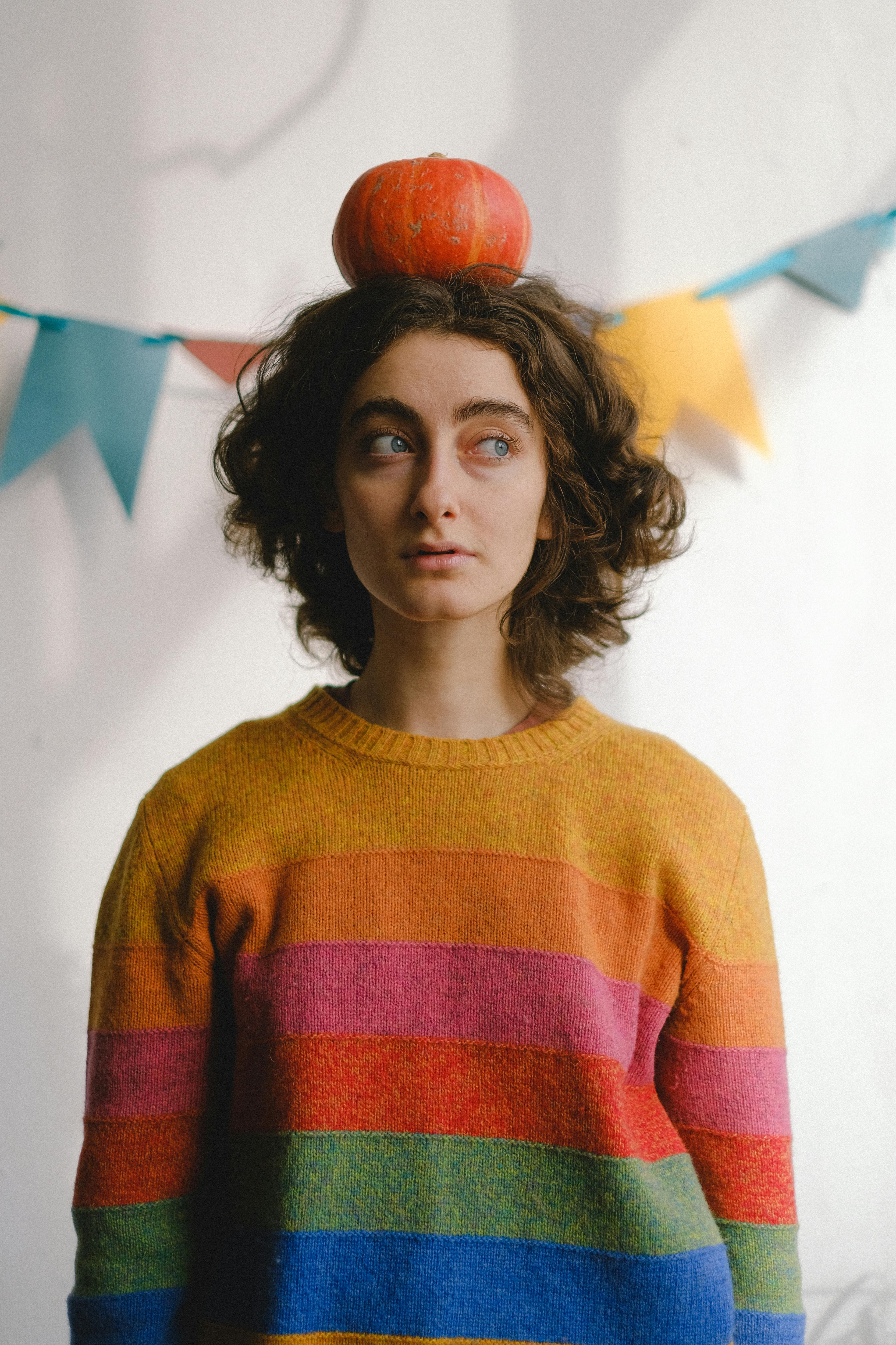 一位穿着彩虹毛衣的女人在室内用头顶着南瓜