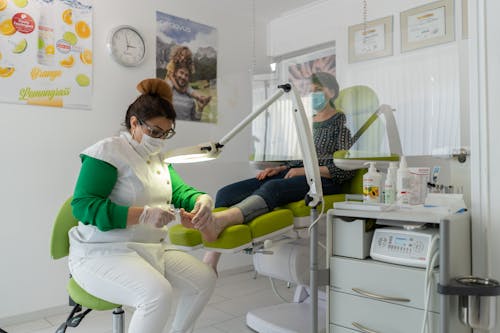 Concentrated professional beauty master in protective mask and gloves doing pedicure in modern salon