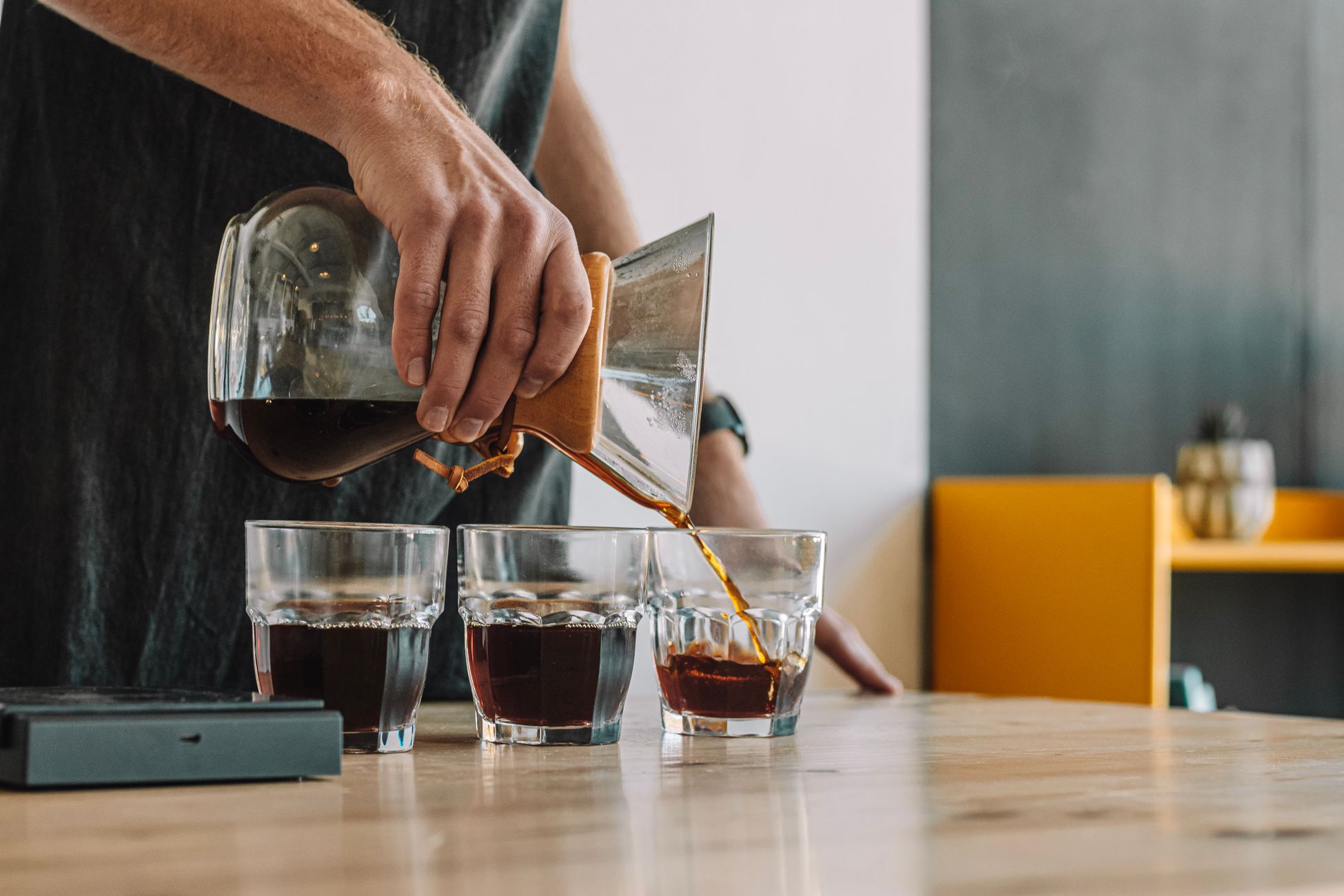 A barista pours coffee into glasses using a Chemex in a modern café.