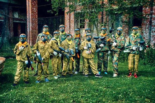 Group of paintball players wearing camouflage gear and masks, holding paintball guns outdoors.