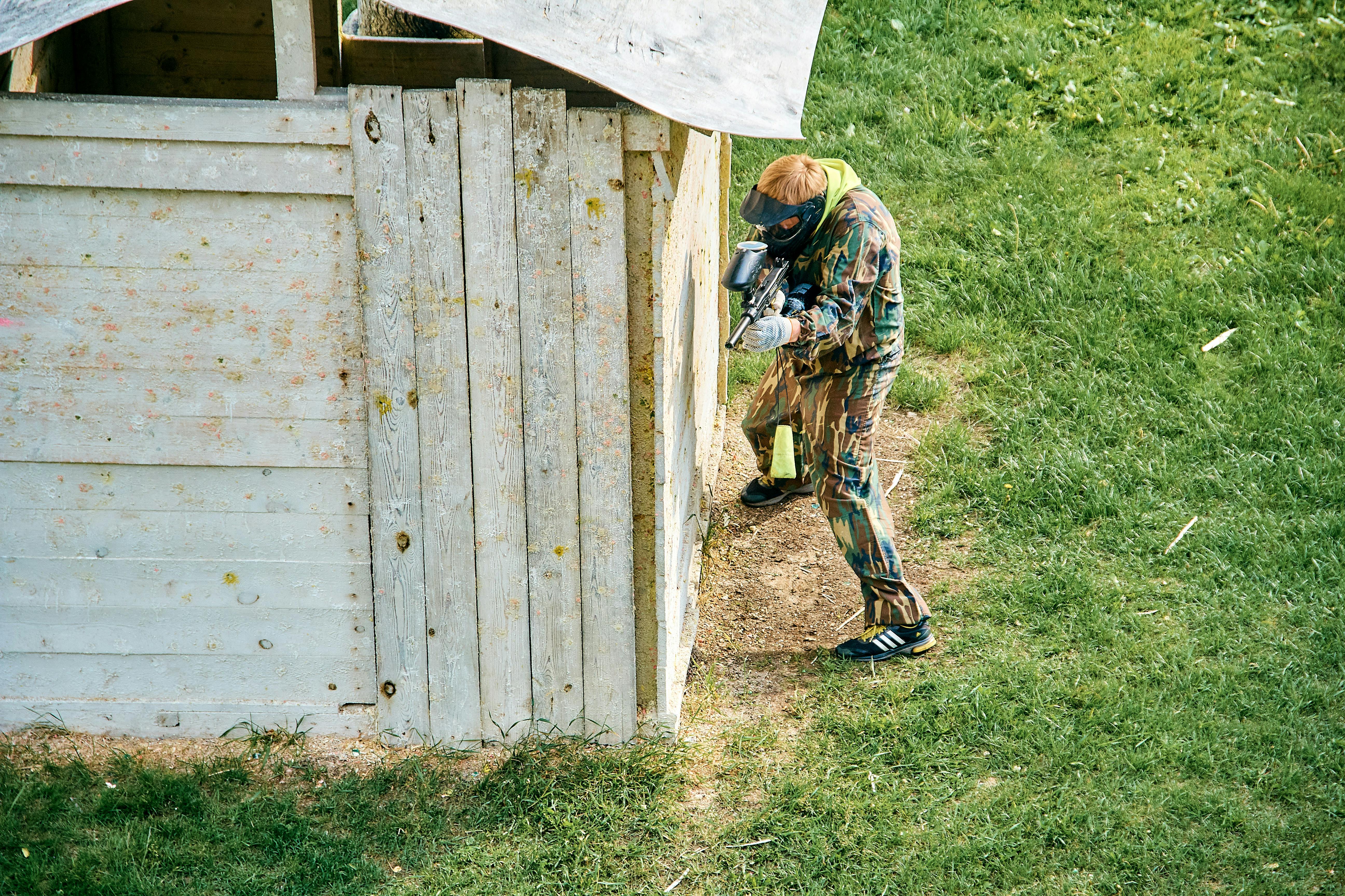 A paintball player taking cover behind a wooden structure on a grassy field during a game. Prescription Goggle Inserts - A paintball player taking cover behind a wooden structure on a grassy field during a game.