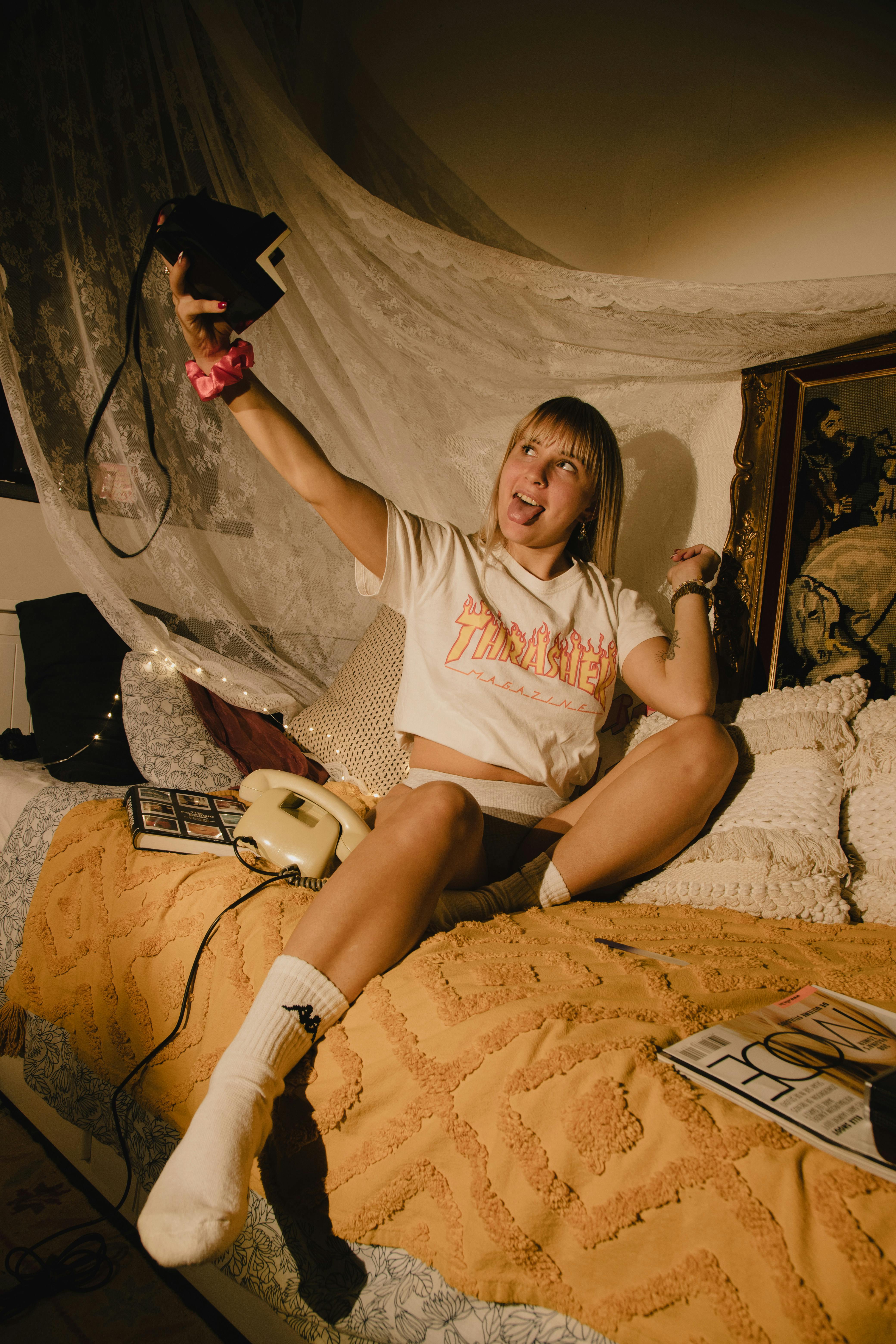 Smiling woman takes a selfie while sitting comfortably in a vintage-styled bedroom.