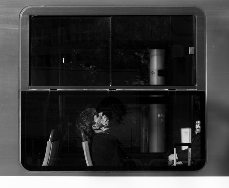 A man in a face mask resting on a train, captured in grayscale.