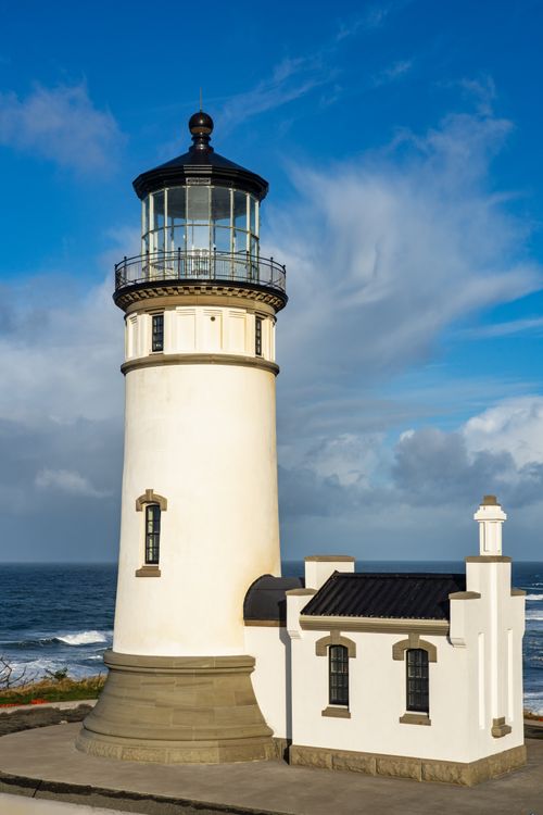 Free A scenic view of a traditional lighthouse against a bright blue sky by the ocean. Stock Photo