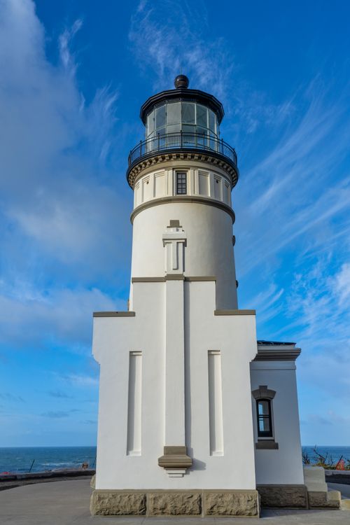 Free Explore the serene beauty of a classic lighthouse standing tall against a vibrant blue sky and ocean backdrop. Stock Photo