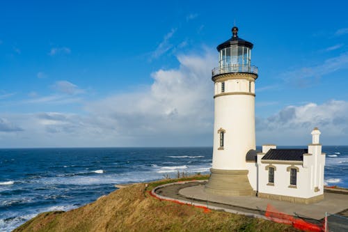 White Lighthouse Near Body of Water Under Blue Sky