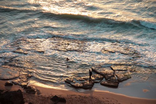 Free A scenic view of a Moroccan beach with waves glistening in the sunlight and people enjoying the surf. Stock Photo