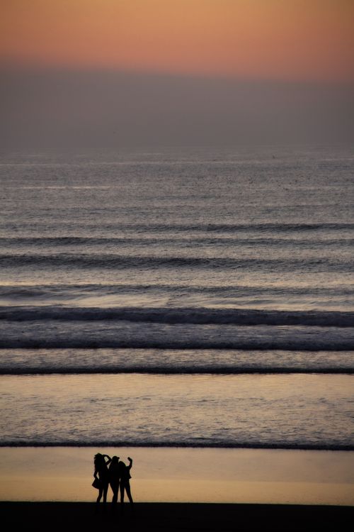Free Silhouette of three friends enjoying the sunset on a picturesque Moroccan beach. Stock Photo