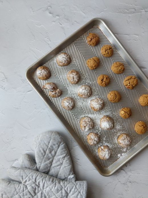 Textured metal half sheet pan of sugared cookies beside grey oven mitts