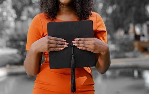 Crop Photo Of Woman in Orange Shirt Holding A Graduation Cap