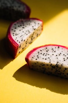 Vibrant dragon fruit slice casting a shadow on a bright yellow surface, highlighting its exotic appeal.
