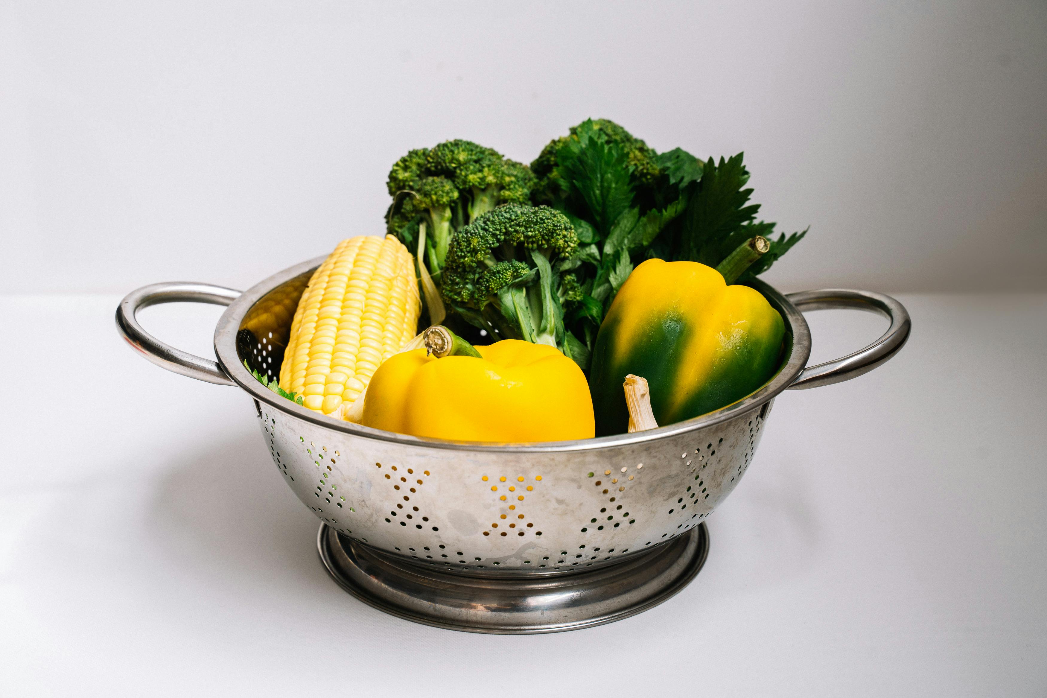 Colorful mix of fresh vegetables in a metal colander, showcasing healthy eating.