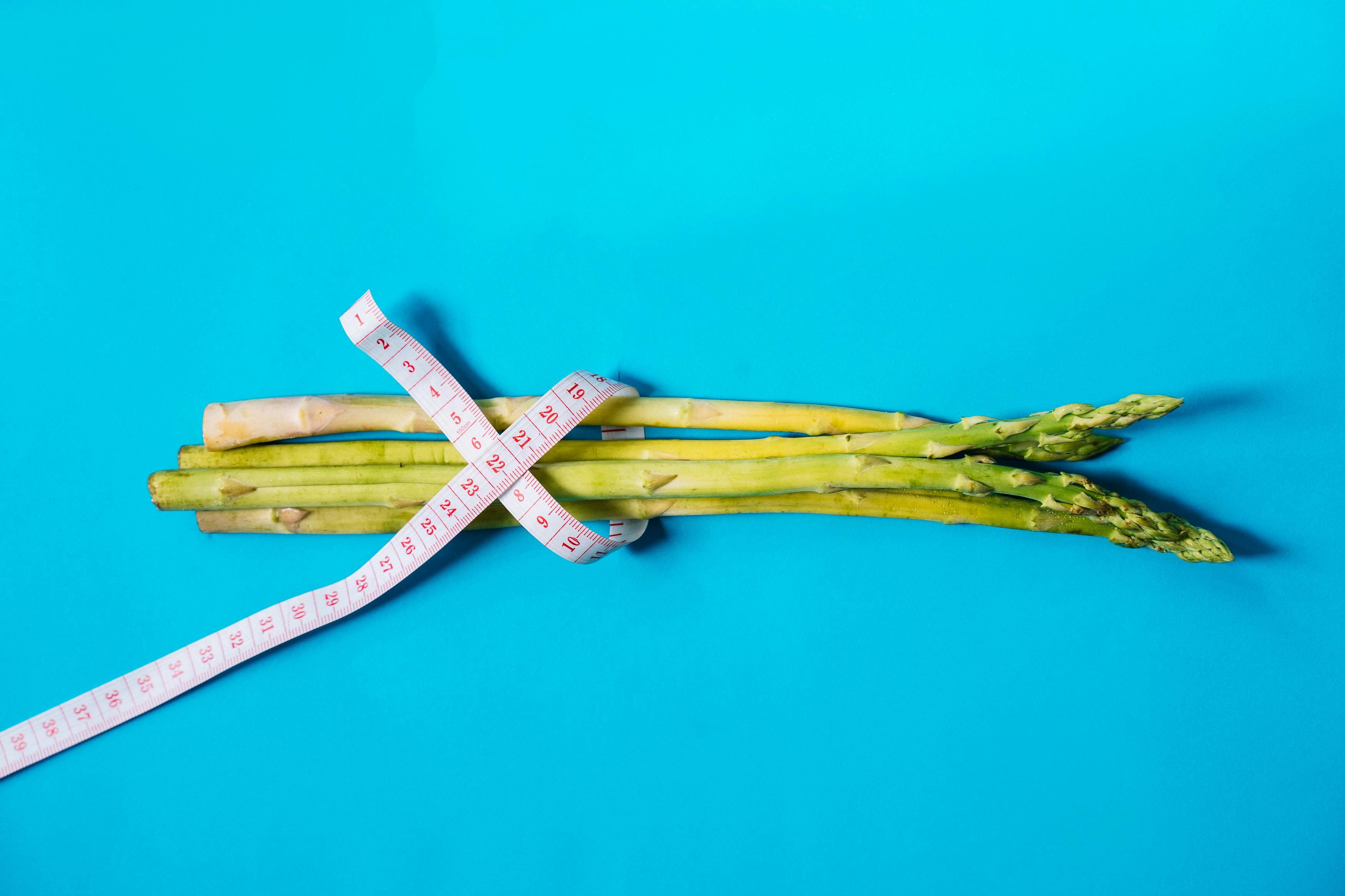 Fresh asparagus wrapped with measuring tape on a vibrant blue background.