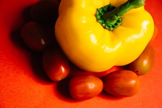 Colorful close-up of yellow bell pepper and cherry tomatoes on red background.