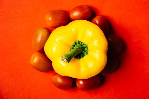 Bright yellow bell pepper with cherry tomatoes on a vivid red background, perfect for food photography.