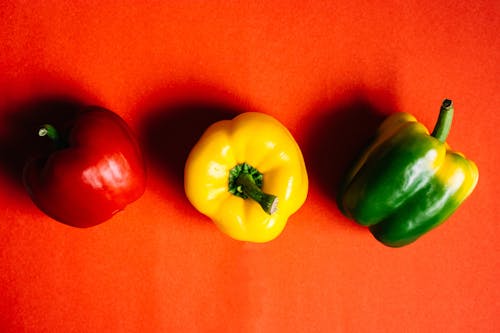 Close-Up Photo of Different Colors of Bell Peppers on Red Background