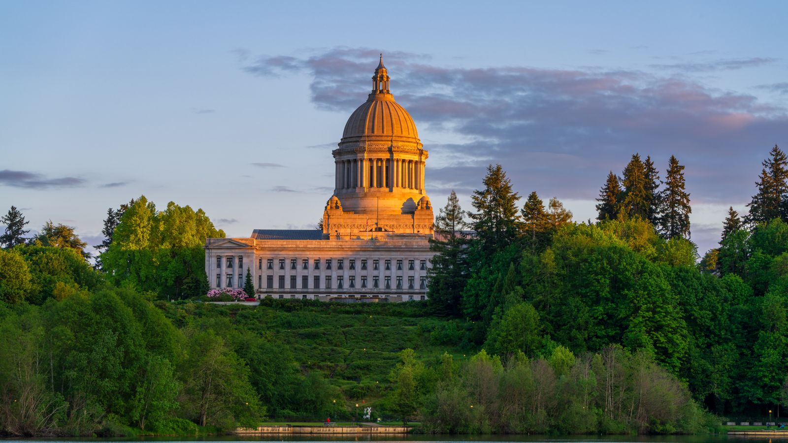 Washington State Capitol Building in Olympia surrounded by lush greenery at sunset.