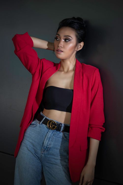 Free Fashionable woman posing in a red jacket and jeans against a dark background. Stock Photo