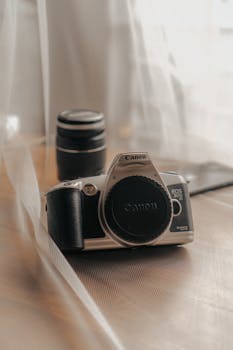 Close-up of a Canon EOS camera with lens, showcasing vintage photography equipment in a soft, moody setting.