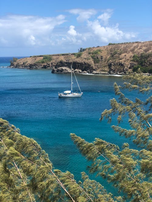 A White Boat on Blue Sea Between Green and Brown Mountains