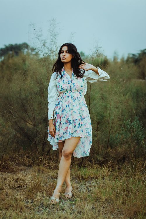 Free Full length of pensive young ethnic lady in romantic dress touching long dark hair while relaxing on grassy meadow in countryside Stock Photo