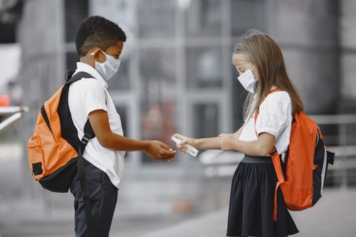 Free Two children wearing masks and backpacks, using sanitizer outdoors. Stock Photo