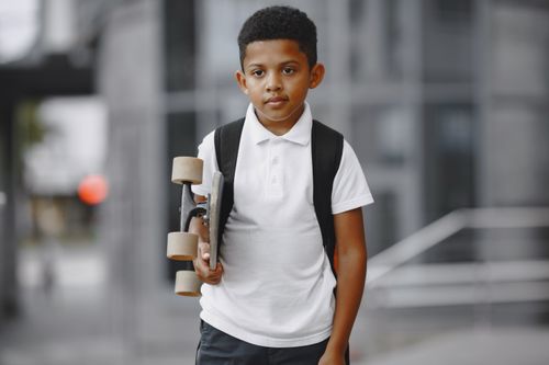 Free A young skateboarder holding a skateboard and wearing a backpack in an urban setting. Stock Photo