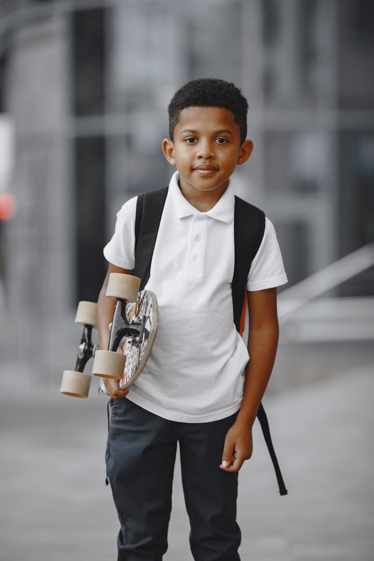 Kid In White Polo Shirt Holding A Skateboard