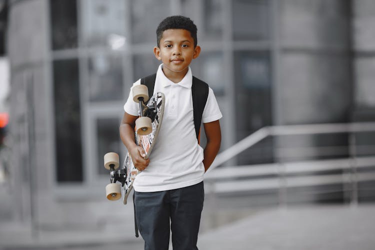 Kid In White Polo Shirt Holding A Skateboard