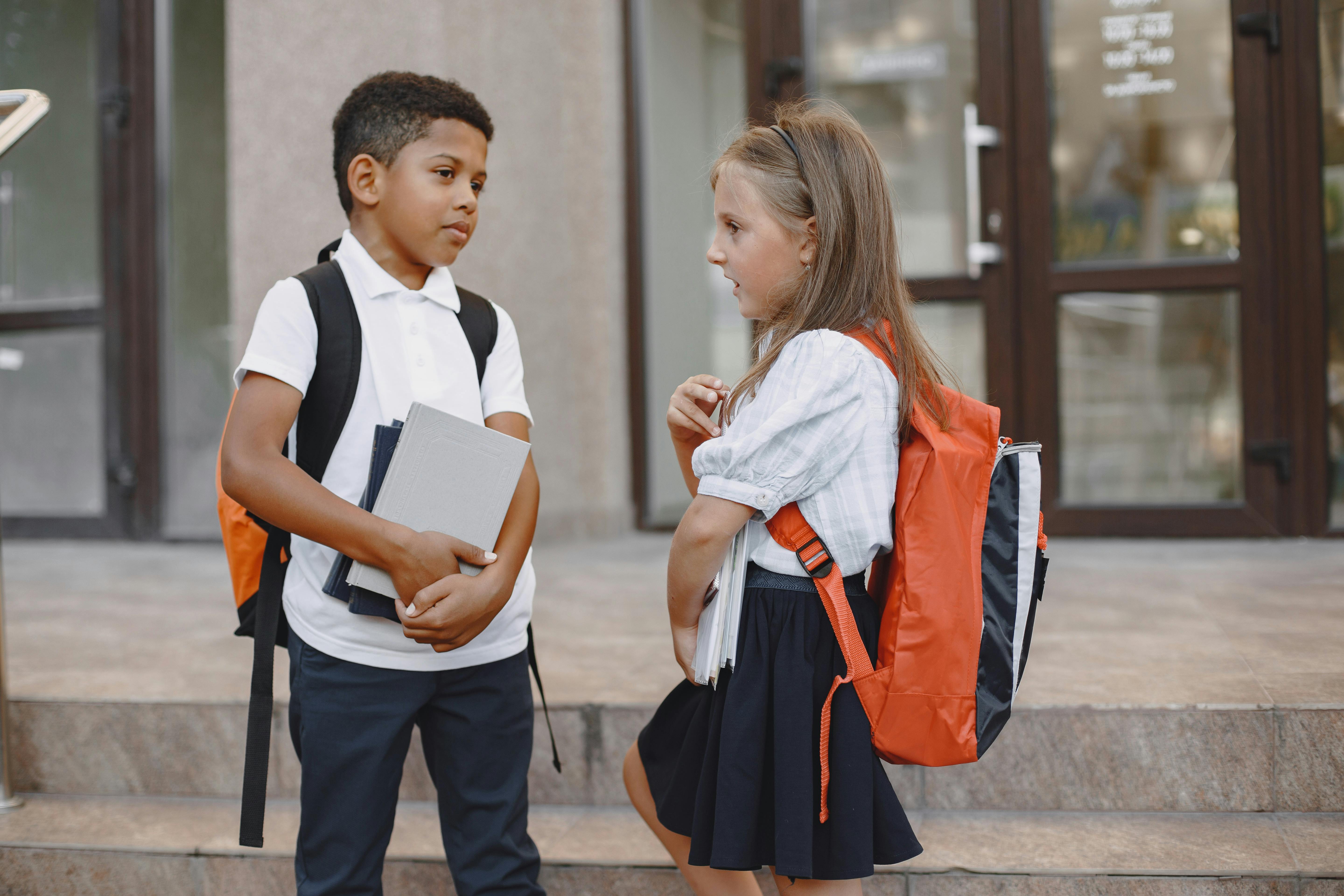 a girl and boy wearing their school uniforms standing on concrete stairs