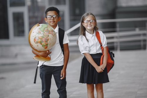 Free Two young students standing outside a school holding a globe, symbolizing education and diversity. Stock Photo