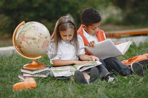 A Boy and a Girl Sitting on Grass with Textbooks and a Globe