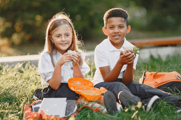 Happy Kids Sitting On Grass Eating Lunch