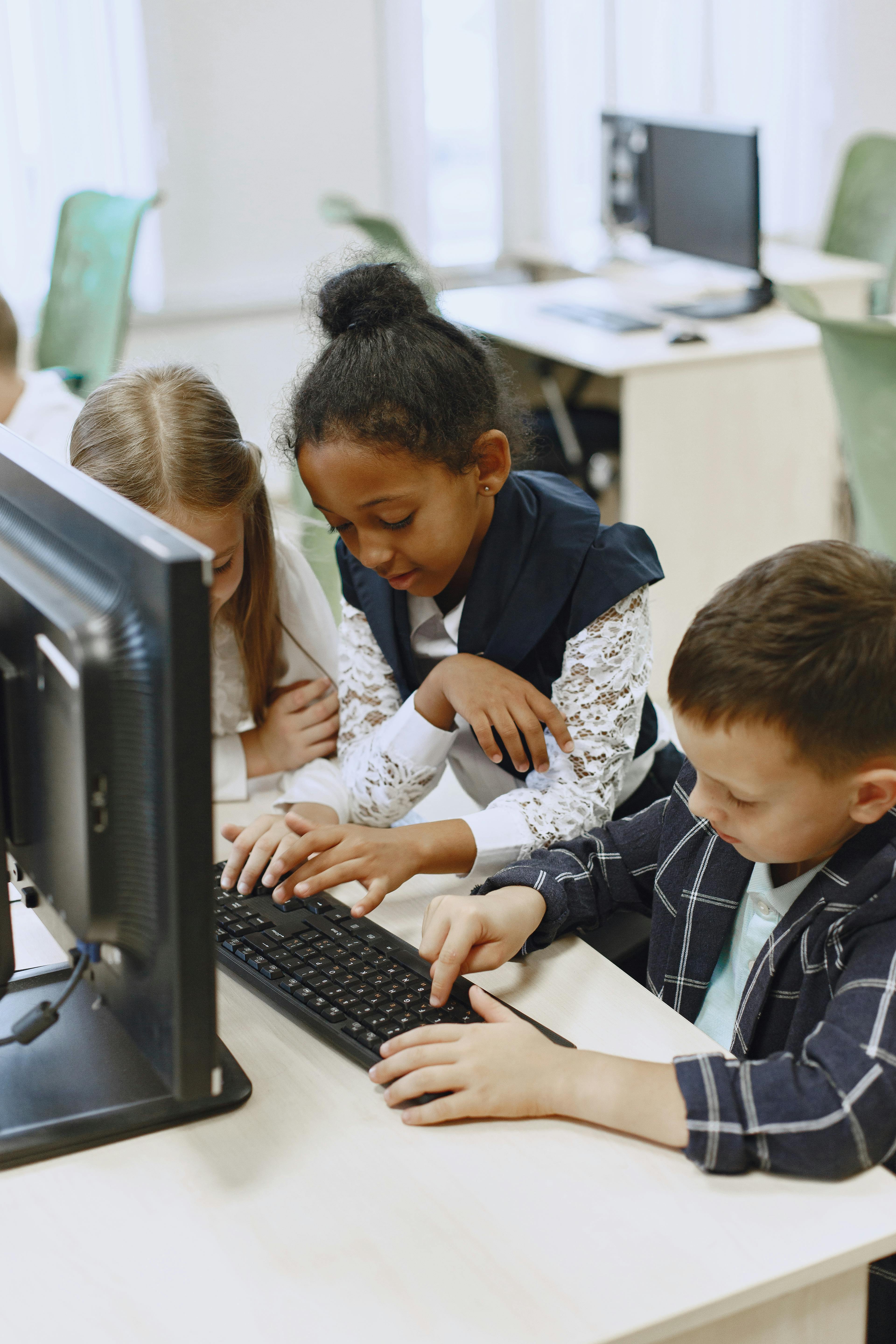 Free Three children work together on a computer in a school lab, learning and collaborating. Stock Photo