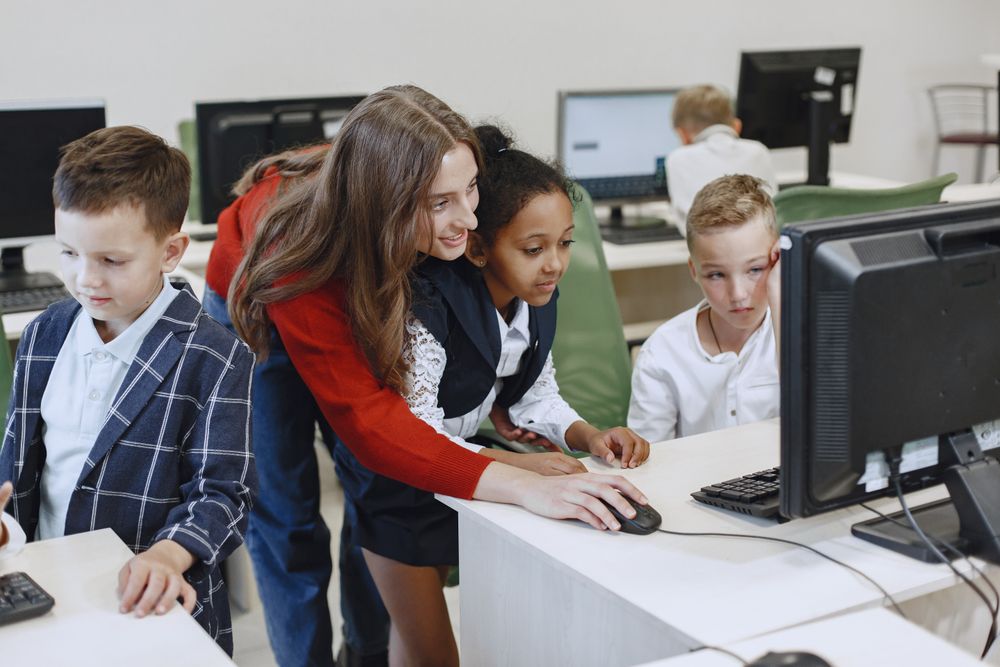 Young diverse primary learners using computers with a teacher in a modern classroom