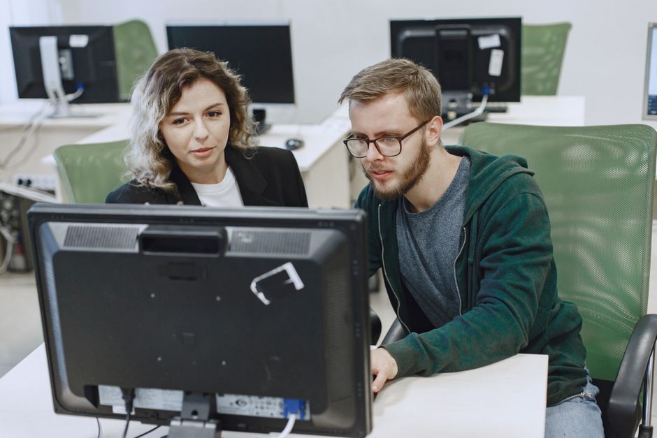 Two colleagues working together on a computer in an office, focusing on a shared task.