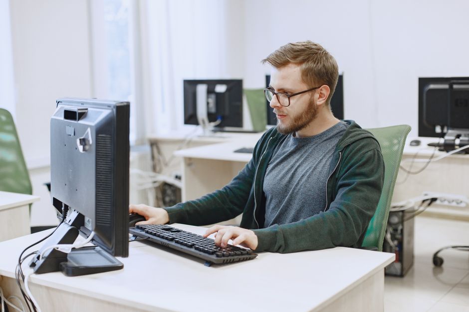 How to Set Up WireGuard VPN Protocol for Faster Mobile Speeds Young man with eyeglasses working on a desktop computer in a modern office environment.